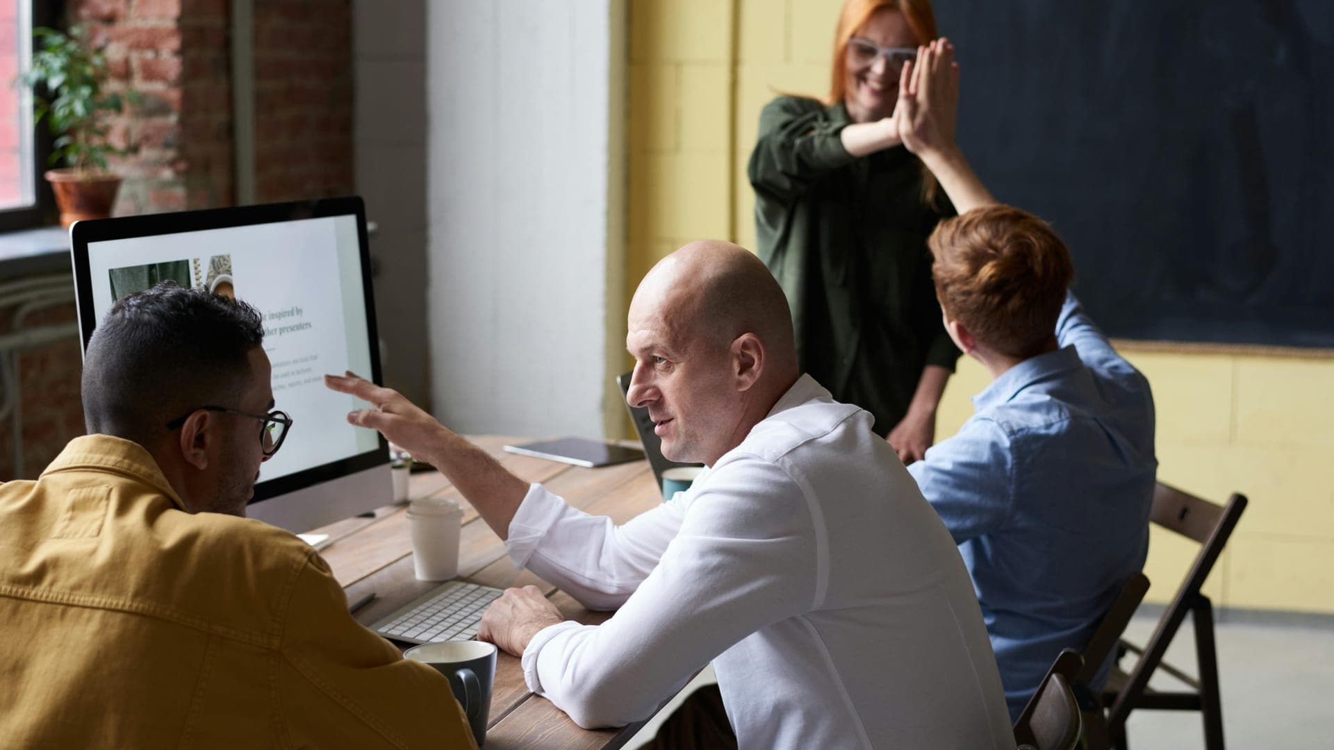 A group of four people engages in a discussion around a table in a bright, modern workspace.