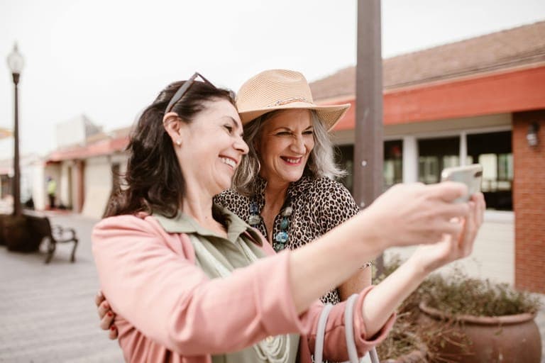 Two women smiling and taking a selfie together outdoors.