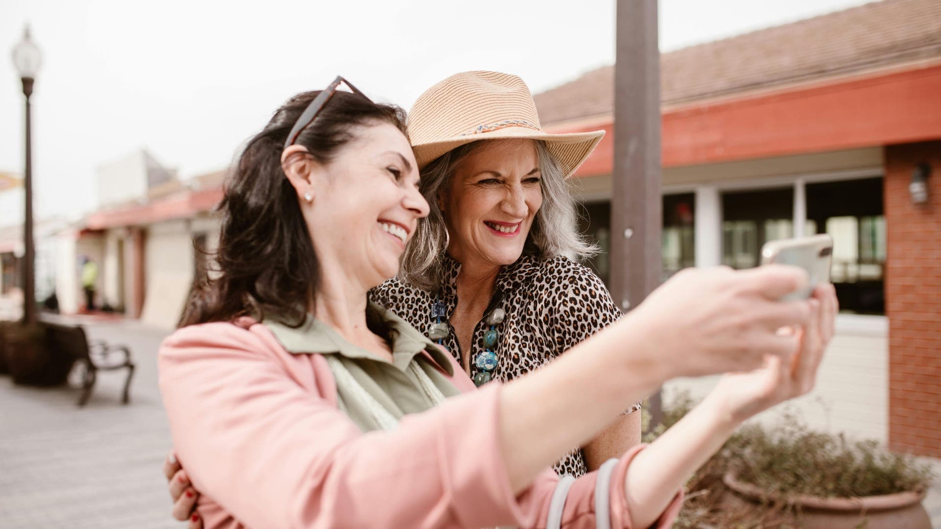 Two women smiling and taking a selfie together outdoors.